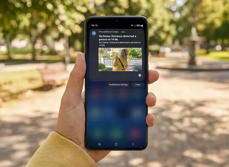 Hand holding smartphone displaying home security alert notification with detected person on video door camera app